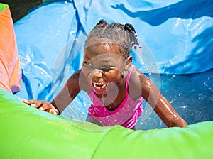 Smiling little girl playing outdoors on an inflatable bounce house water slide