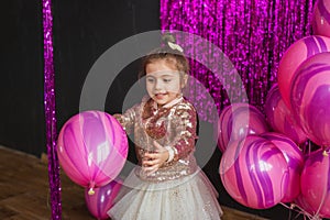 Smiling little girl plays with pink balloons at studio