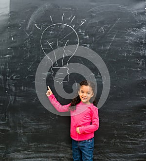 Smiling little girl pointing at drawn on the blackboard lamp