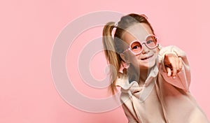 Smiling little girl preschooler with ponytail looking forward pointing index finger at you. Close up shot isolated on pink