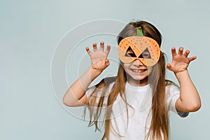 Smiling little girl in a pumpkin mask celebrates Halloween on a blue background.