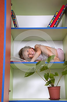 Smiling little girl reading a book in a bookcase
