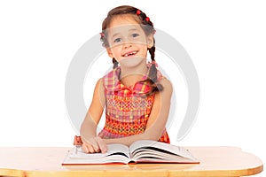 Smiling little girl reading book on the desk