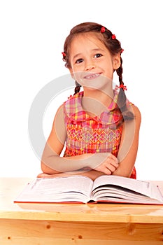 Smiling little girl reading book on the desk