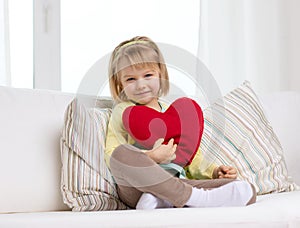 Smiling little girl with red heart at home