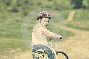 Smiling little girl riding a bike turned away