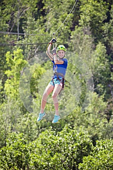 Smiling little girl riding a zipline through the forest