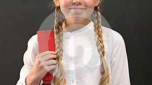 Smiling little girl with rucksack standing against blackboard, ready for school