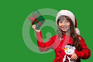 A smiling little girl in a Santa hat shows a beautifully wrapped present. Merry Christmas and Happy New Year 2023