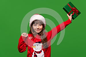 A smiling little girl in a Santa hat shows a beautifully wrapped present. Merry Christmas and Happy New Year 2023