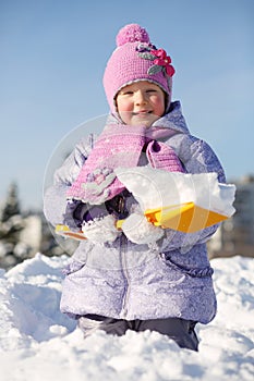 Smiling little girl with shovel shows snow in snowdrift