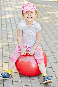 Smiling little girl sits on red ball for jumping