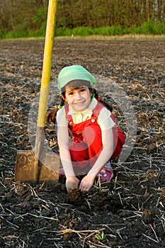 Smiling little girl sitting on field with shovel