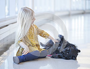 Smiling little girl sitting on floor and patting black dog