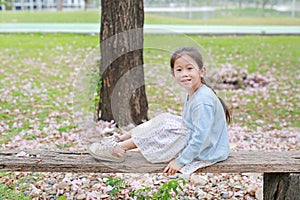 Smiling little girl sitting on wood logs against falling pink flower in the summer garden
