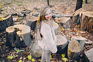 Smiling little girl stand next to wooden stumps in the forest at autumn day.