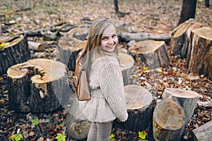 Smiling little girl stand next to wooden stumps in the forest at autumn day.