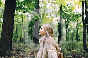 Smiling little girl stand is walking in the forest at autumn day.