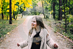 Smiling little girl stand is walking in the forest at autumn day.