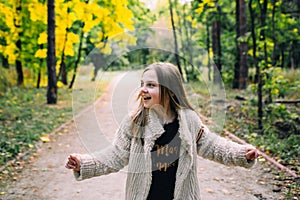 Smiling little girl stand is walking in the forest at autumn day.