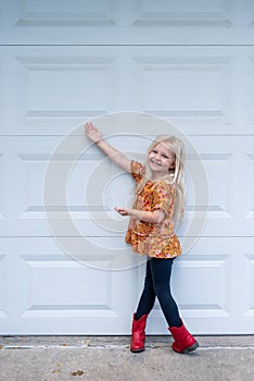 Smiling little girl standing in the driveway in red cowboy boots