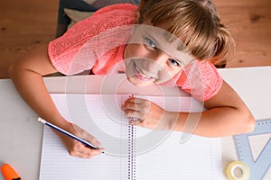 Smiling little girl studying in room on desk with school supplies looking top