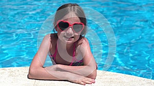 Smiling little girl in sunglasses in pool on sunny day. Childhood, valentine's day and summer concept