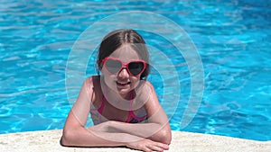 Smiling little girl in sunglasses in pool on sunny day. Happy kid having fun outdoors on holidays