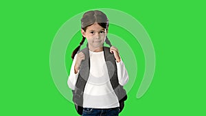 Smiling little girl walking to school holding her backpack and looking at camera on a Green Screen, Chroma Key.