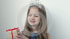 Smiling little girl wearing princess crown and blue festive dress shows a gift