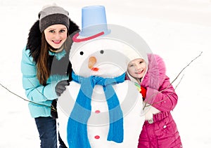 Smiling little girl and young woman with snowman in winter day