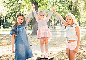 Smiling little girls stand with joyfully raised hands in park