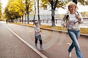 Smiling little kid boy and his grandmother having fun in autumn park, grandson runs after grandparent