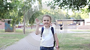 Smiling little kid elementary schoolgirl waving hand say goodbye while standing at school entrance. School concept