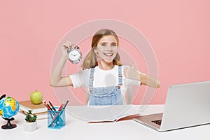 Smiling little kid schoolgirl 12-13 years old sit study at desk with laptop isolated on pink background. School distance