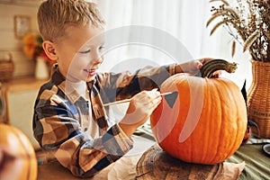 Smiling little kids boy making jack-o-lantern at home, drawing scary face on pumpkin