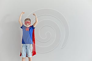 Smiling little superhero shows his muscles on a background of a gray wall.