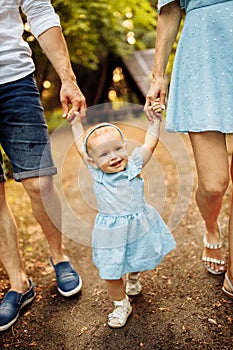 Smiling little toddler making first steps holding parents hands, cute baby girl in blue dress with mom and dad walk at