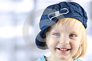 Smiling llittle girl with a cap on her head on a blue background