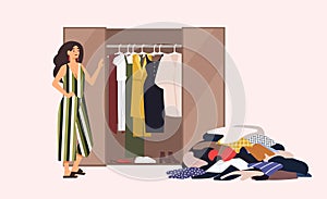 Smiling long-haired girl standing in front of opened closet with apparel hanging inside and pile of clothes on floor photo