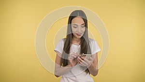 Smiling long-haired woman middle age with a smartphone having thumbs up on yellow background in studio. Middleweight