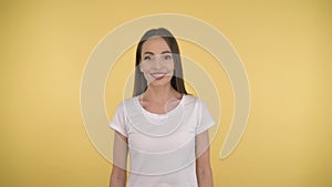 Smiling long-haired woman middle age on yellow background in studio. Middleweight woman in basic white t-shirt