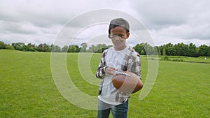 Smiling lovely black school boy with american football ball on pitch