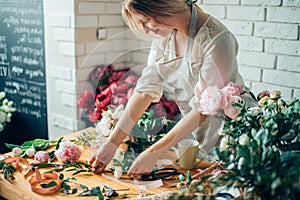 Smiling lovely young woman florist arranging plants in flower shop photo