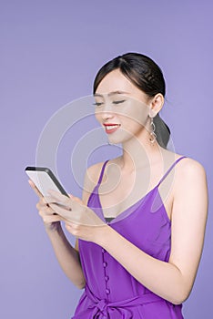 Smiling lovely young woman standing and using cell phone over violet background