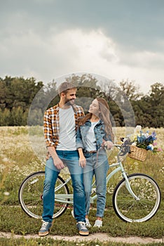 smiling lovers with retro bicycle looking at each other in field