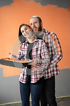 Smiling loving couple doing home renovations, woman holding tray and paint roller, man hug her