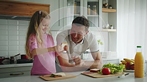 The smiling loving father and daughter standing in the kitchen at the table, he helps cooking sandwiches, hugs and