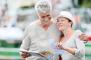 Smiling loving senior couple using map and tablet visiting