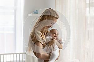 Smiling loving young mother holding baby, standing at home